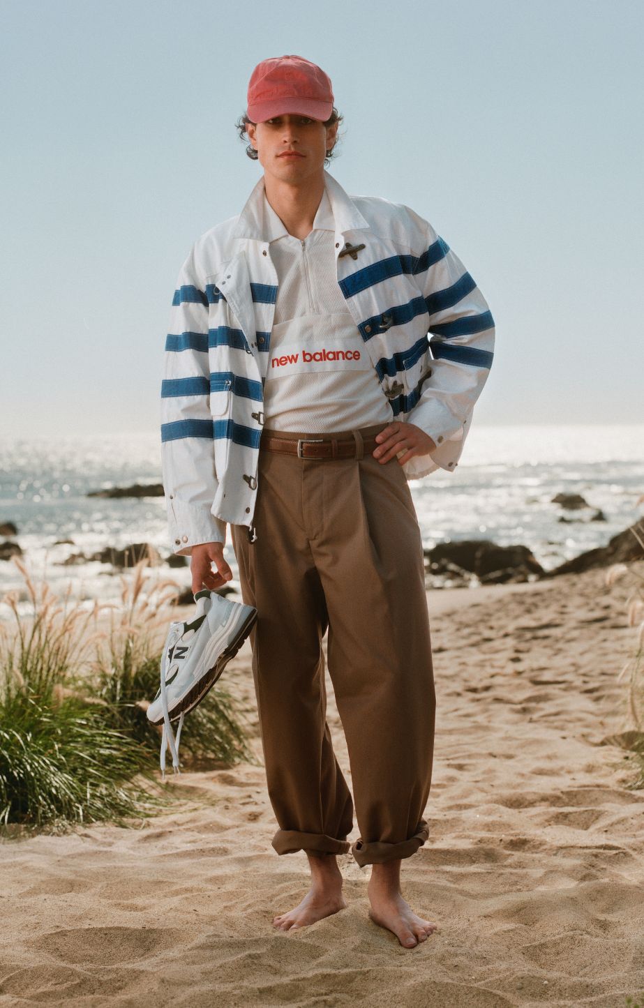 A man standing on the sand, holding made in usa 992 sneakers